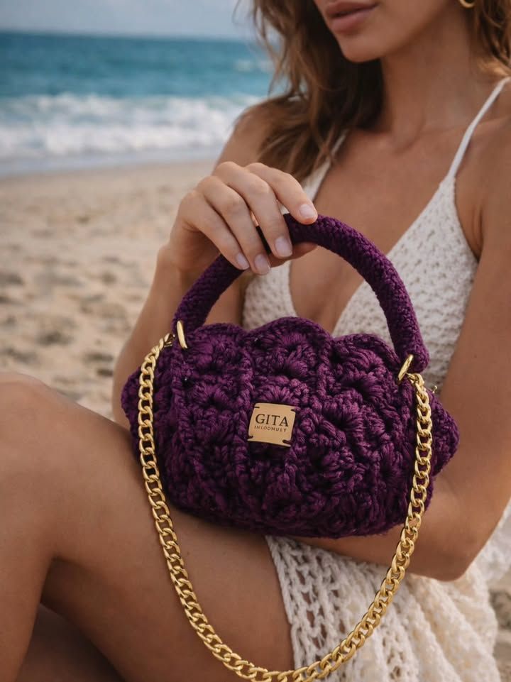 Bolsa de crochê roxa em fio de malha de algodão, com ponto concha, alça de corrente dourada e etiqueta de couro GITA, na praia